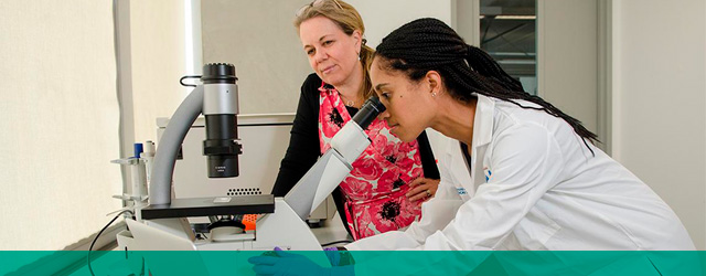 student examining speciman through microsope while advisor observes
